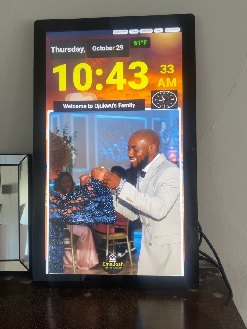 An EmaJosh home screen displaying family wedding memories, a large digital clock, date and weather in a living space